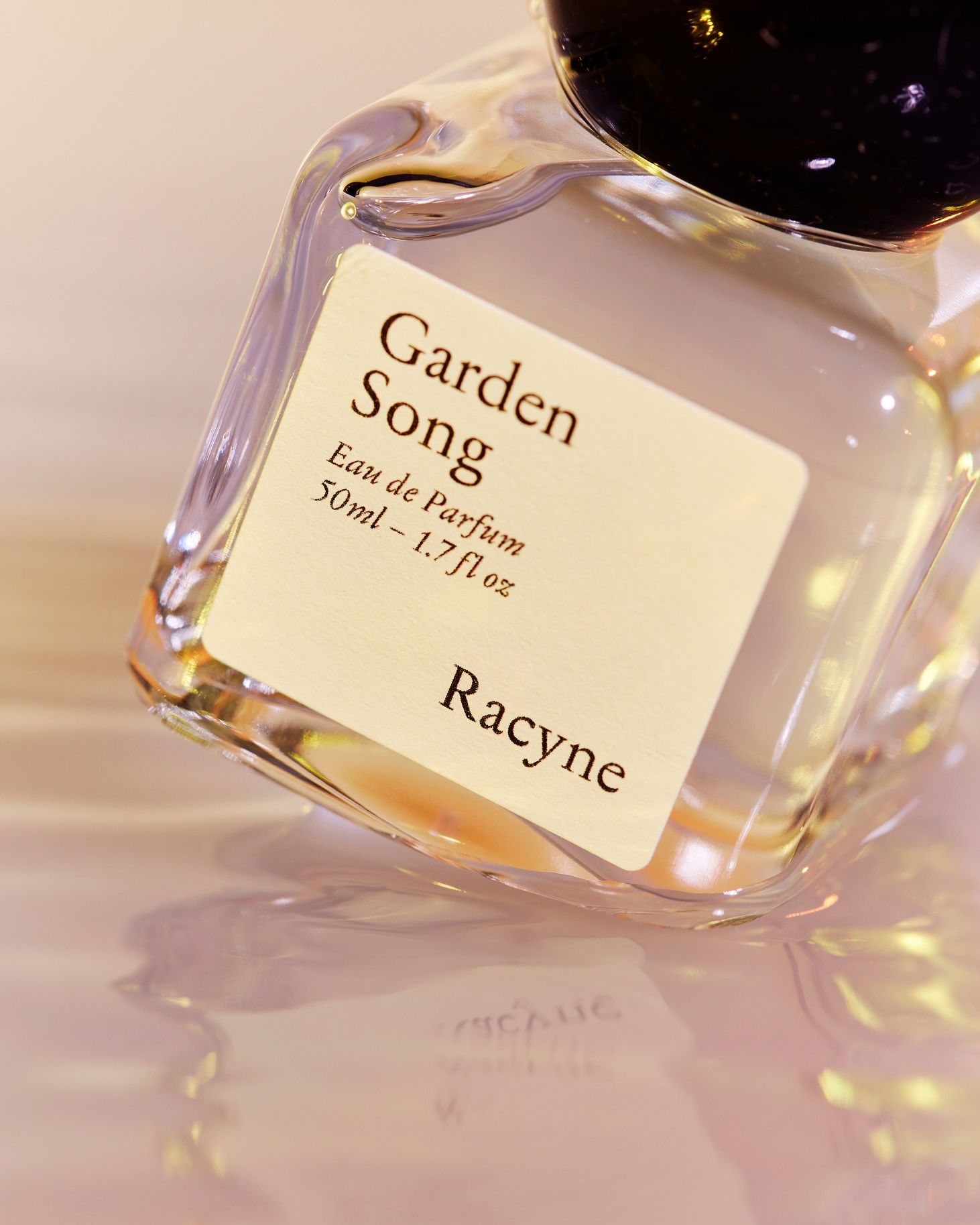 Close-up of a glass perfume bottle with a black cap and a white label that reads "Garden Song Eau de Parfum" and the brand "Racyne."