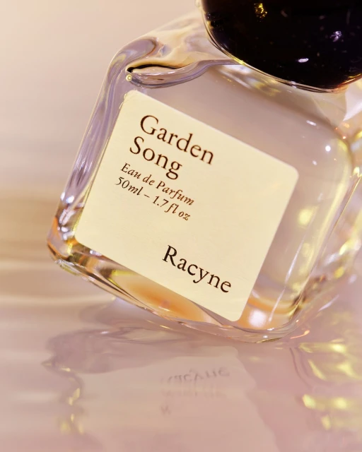 Close-up of a glass perfume bottle with a black cap and a white label that reads "Garden Song Eau de Parfum" and the brand "Racyne."