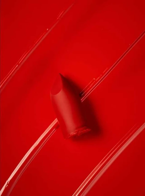 Close-up studio shot of red lipstick on a glossy red surface with linear swipes, showcasing color and texture for beauty advertising.
