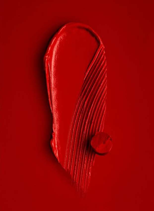 Close-up of red lipstick smear and drop on a red background. Beauty photography. Makeup advertising. Bright, vivid color.