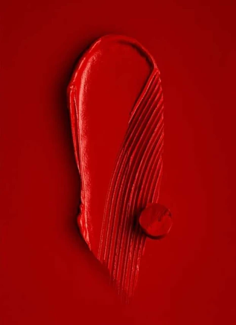 Close-up of red lipstick smear and drop on a red background. Beauty photography. Makeup advertising. Bright, vivid color.