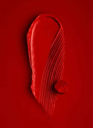 Close-up of red lipstick smear and drop on a red background. Beauty photography. Makeup advertising. Bright, vivid color.