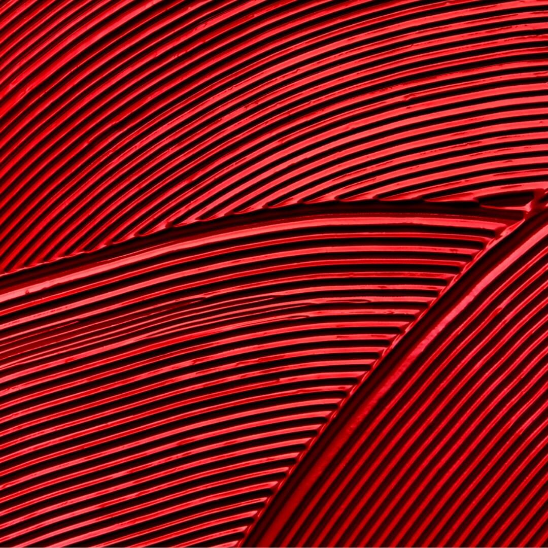 Abstract view of curved parallel lines on a textured surface with dark shadows, bathed in a dominant red color scheme.