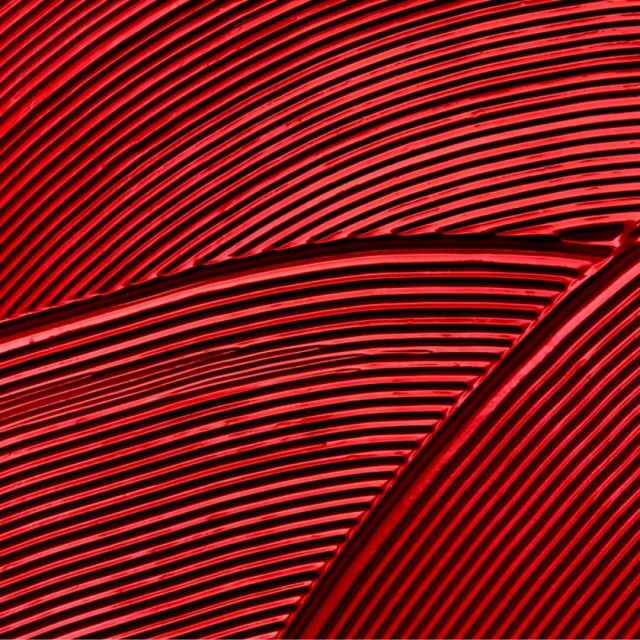 Abstract view of curved parallel lines on a textured surface with dark shadows, bathed in a dominant red color scheme.