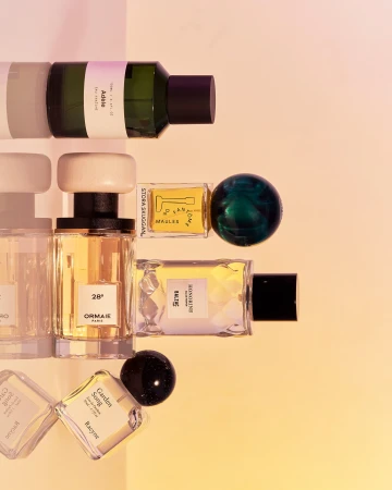 Several perfume bottles with white and black caps arranged against a warm gradient background