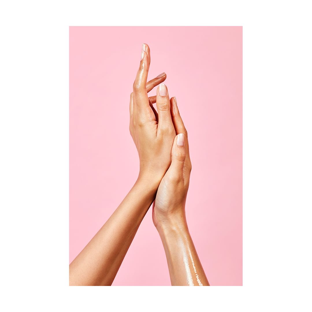 Close-up studio shot of two female arms overlapping against a pink background, showcasing beauty and skincare, with visible skin texture.