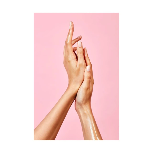 Close-up studio shot of two female arms overlapping against a pink background, showcasing beauty and skincare, with visible skin texture.
