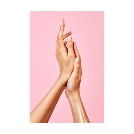 Close-up studio shot of two female arms overlapping against a pink background, showcasing beauty and skincare, with visible skin texture.