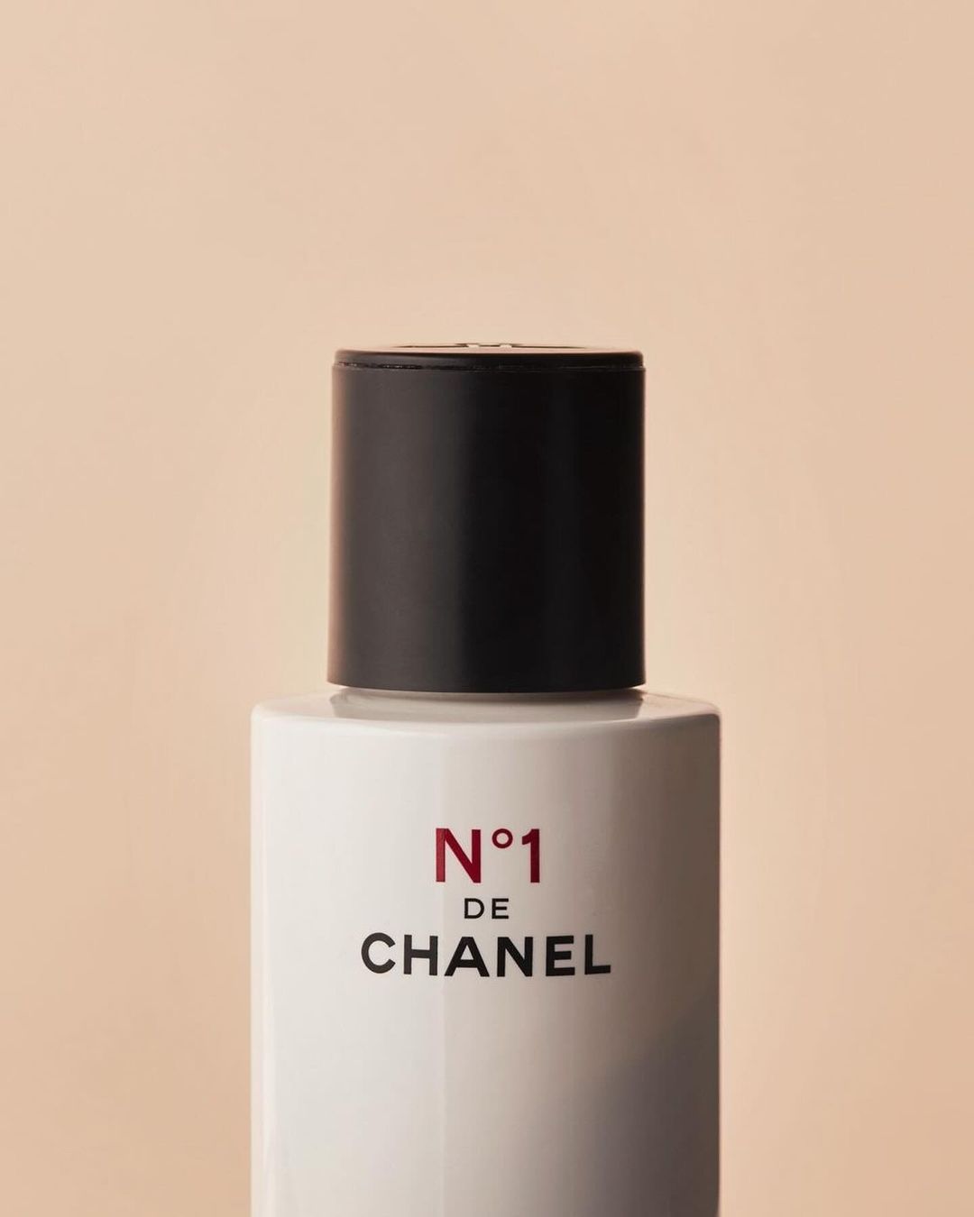 Close-up of a white Chanel N°1 bottle with a black cap against a light peach background, showcasing minimalist beauty and elegant design.