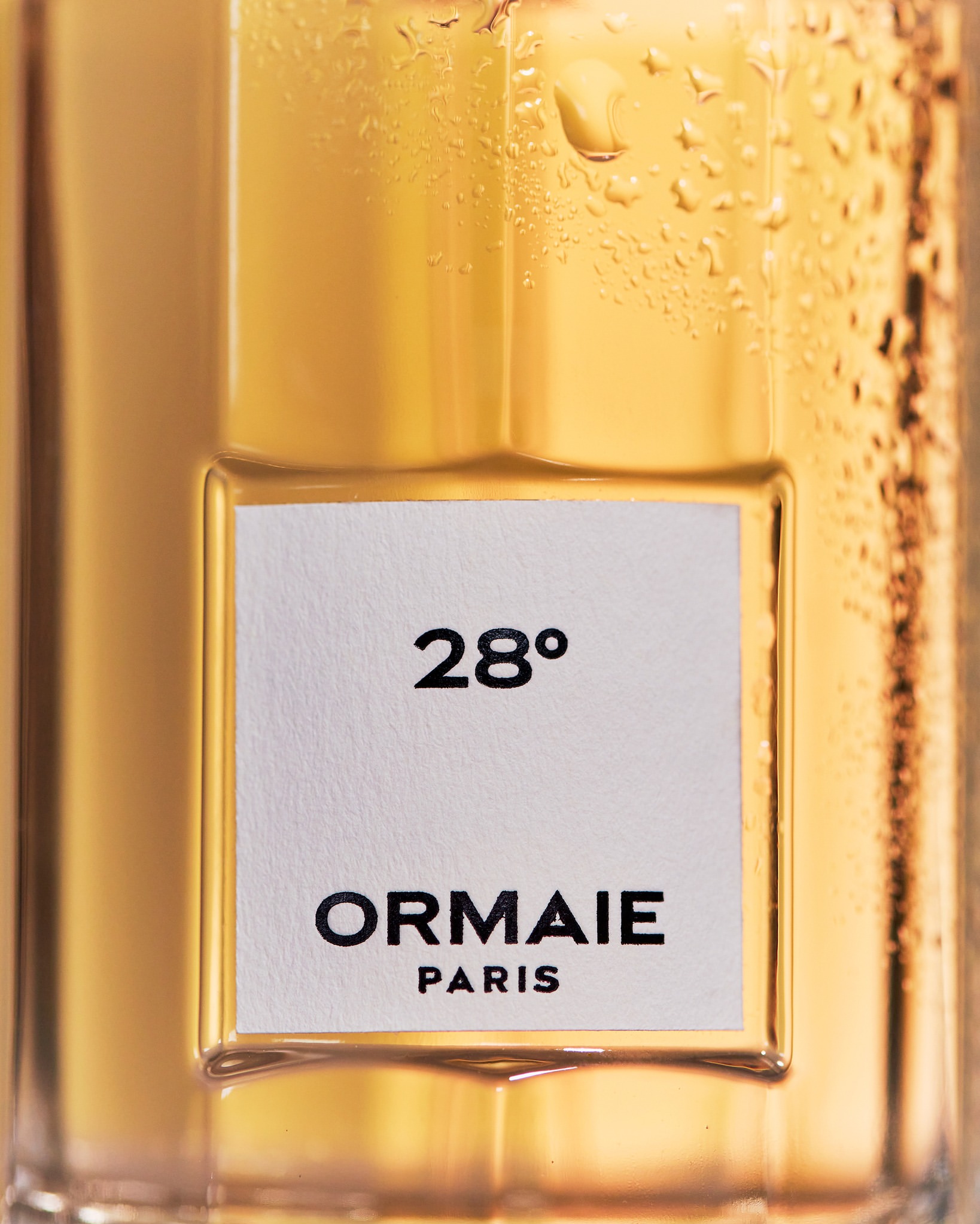 Close-up of a clear glass bottle with water droplets and a white label featuring black text that reads '28°' and 'ORMAIE PARIS'.