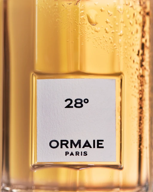 Close-up of a clear glass bottle with water droplets and a white label featuring black text that reads '28°' and 'ORMAIE PARIS'.