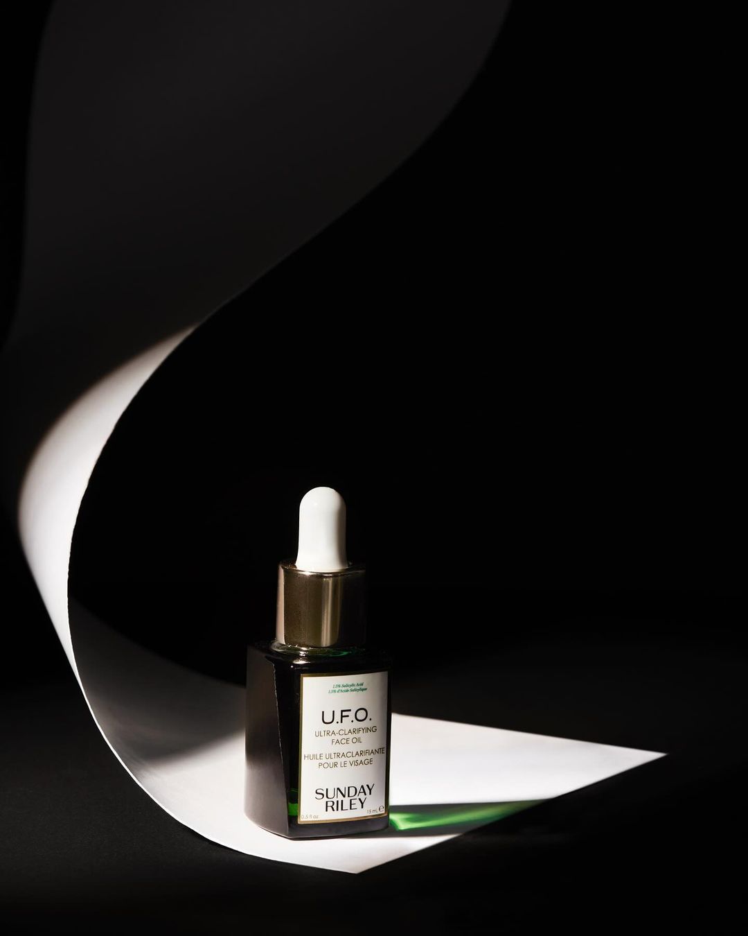 Studio shot of Sunday Riley U.F.O. Ultra-Clarifying Face Oil, against a black background with a curved white paper accent.