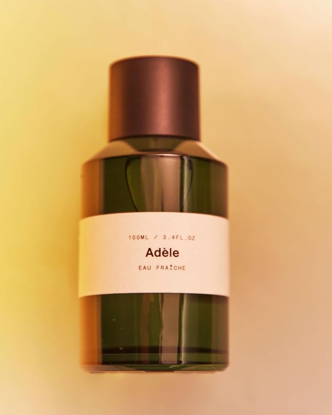 Close-up studio shot of an Adèle Eau Fraîche perfume bottle featuring a cylindrical form, dark brown cap, and a minimalist label.