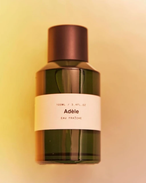 Close-up studio shot of an Adèle Eau Fraîche perfume bottle featuring a cylindrical form, dark brown cap, and a minimalist label.