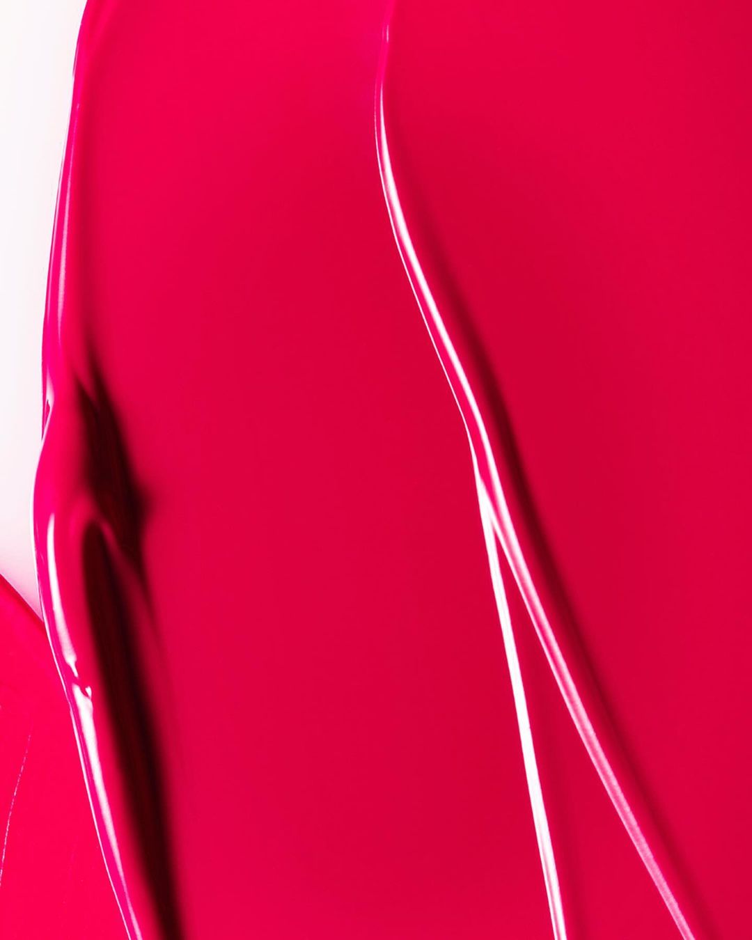 Close-up shot of a glossy, vibrant magenta-colored cosmetic product with smooth textures and bright reflections on a light background.