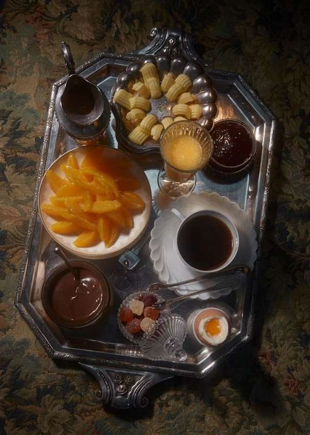 Overhead shot of silver tray featuring a variety of breakfast items: orange slices, small pastries, juice, jam, coffee, fruit, and a boiled egg.