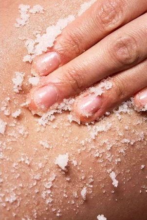 Close-up of a person's hand gently exfoliating skin with a grainy scrub, highlighting skincare and the texture of the product.