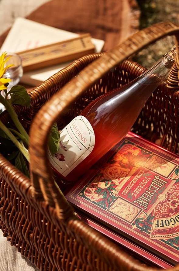 Picnic basket with rose wine, a sunflower, and books, set on a blanket for an outdoor gathering, inviting a relaxed, celebratory mood.