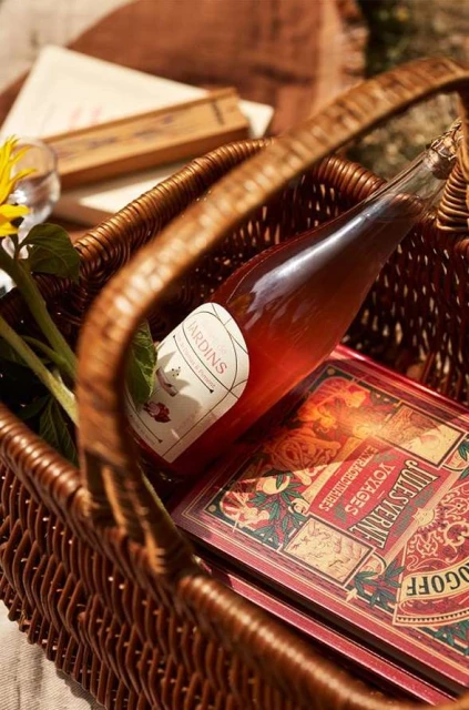 Picnic basket with rose wine, a sunflower, and books, set on a blanket for an outdoor gathering, inviting a relaxed, celebratory mood.