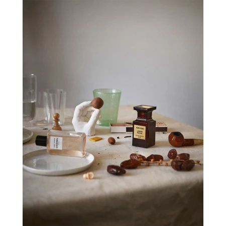 Still life tabletop arrangement of perfume bottles, glass objects, dates, and a hand sculpture on a beige tablecloth.