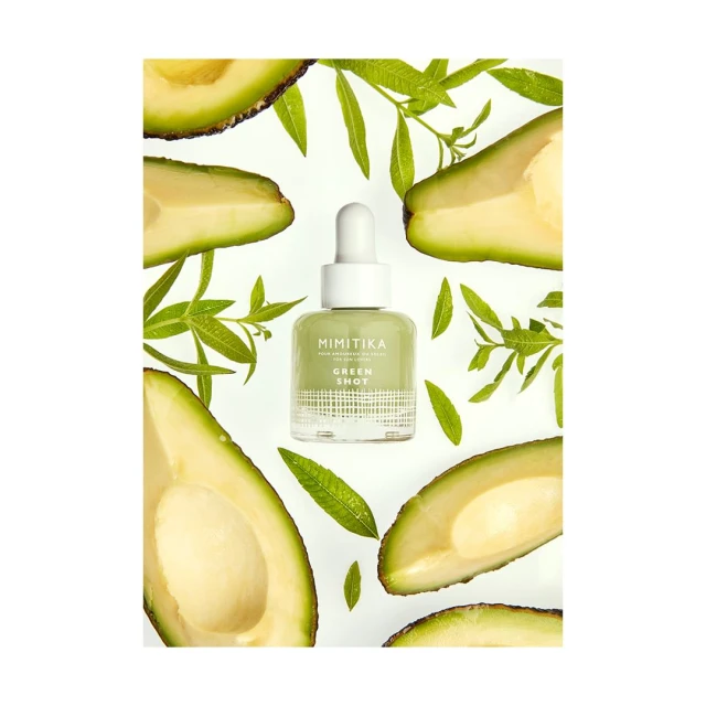 Product shot of Mimikita Green Shot serum bottle surrounded by avocado slices and green leaves, set against a white background.