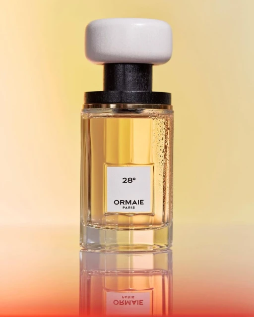 Product shot of a glass perfume bottle with a white cap, featuring the brand ORMAIE PARIS, set against a gradient yellow background.