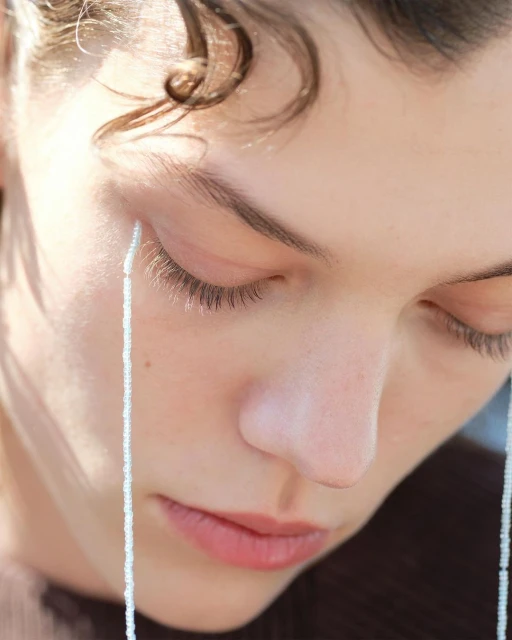 Close-up portrait of a fair-skinned young woman with light brown hair, closed eyes, and beaded strands hanging near her face.
