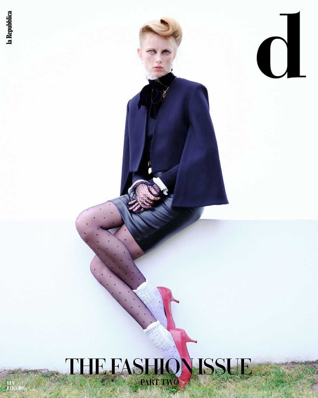 Fashion editorial shot of a posed female model in vintage-inspired attire, seated against a white background with a grassy edge, magazine cover.