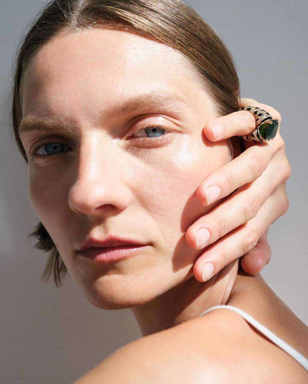 Close-up shot of a fair-skinned adult woman with hand near her face, showcasing a statement ring on her finger, in soft natural lighting.