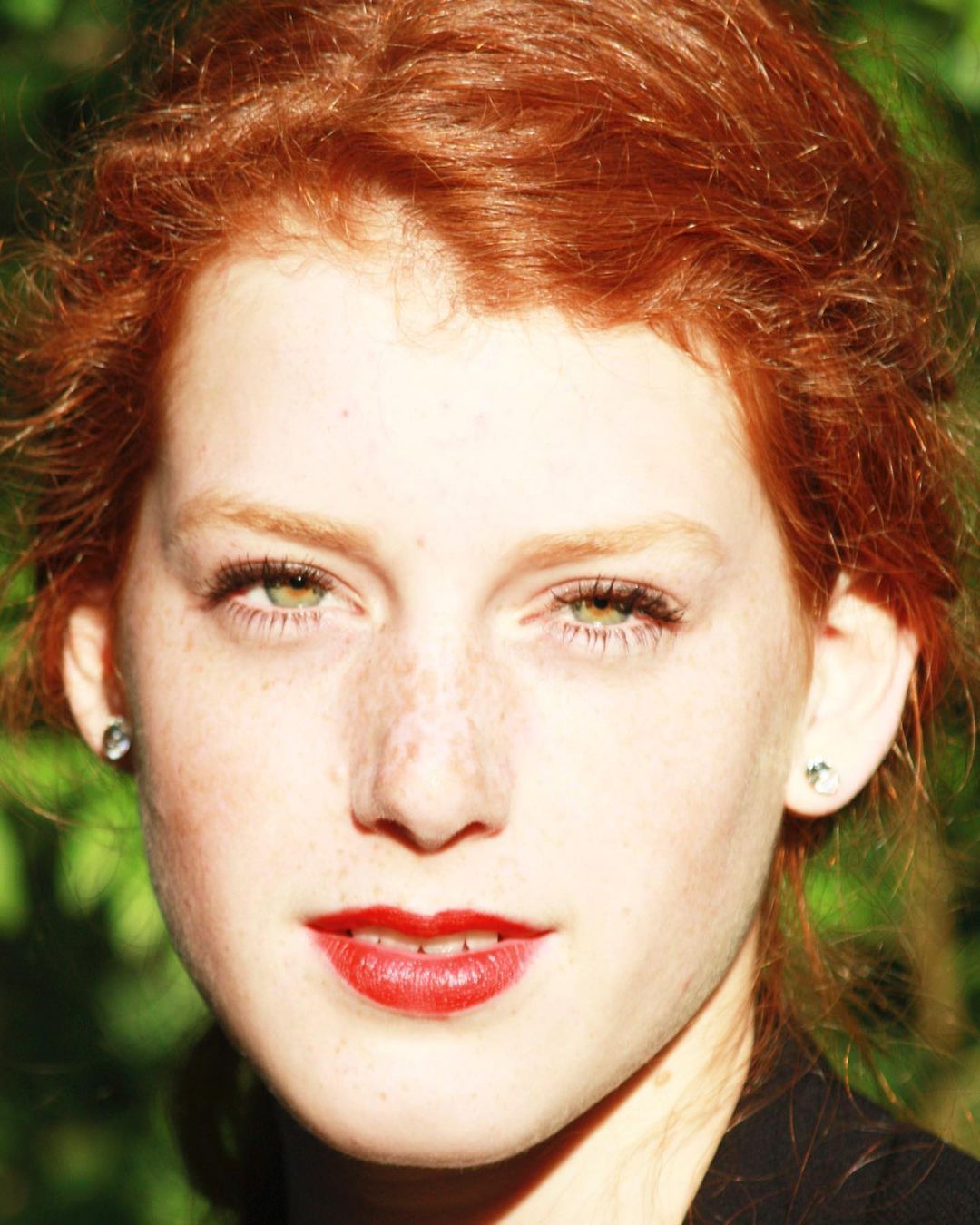 Close-up portrait of a young woman with vibrant red hair, green eyes, and freckles against a natural background by Liv Liberg