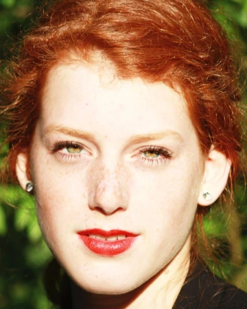 Close-up portrait of a young woman with vibrant red hair, green eyes, and freckles against a natural background by Liv Liberg