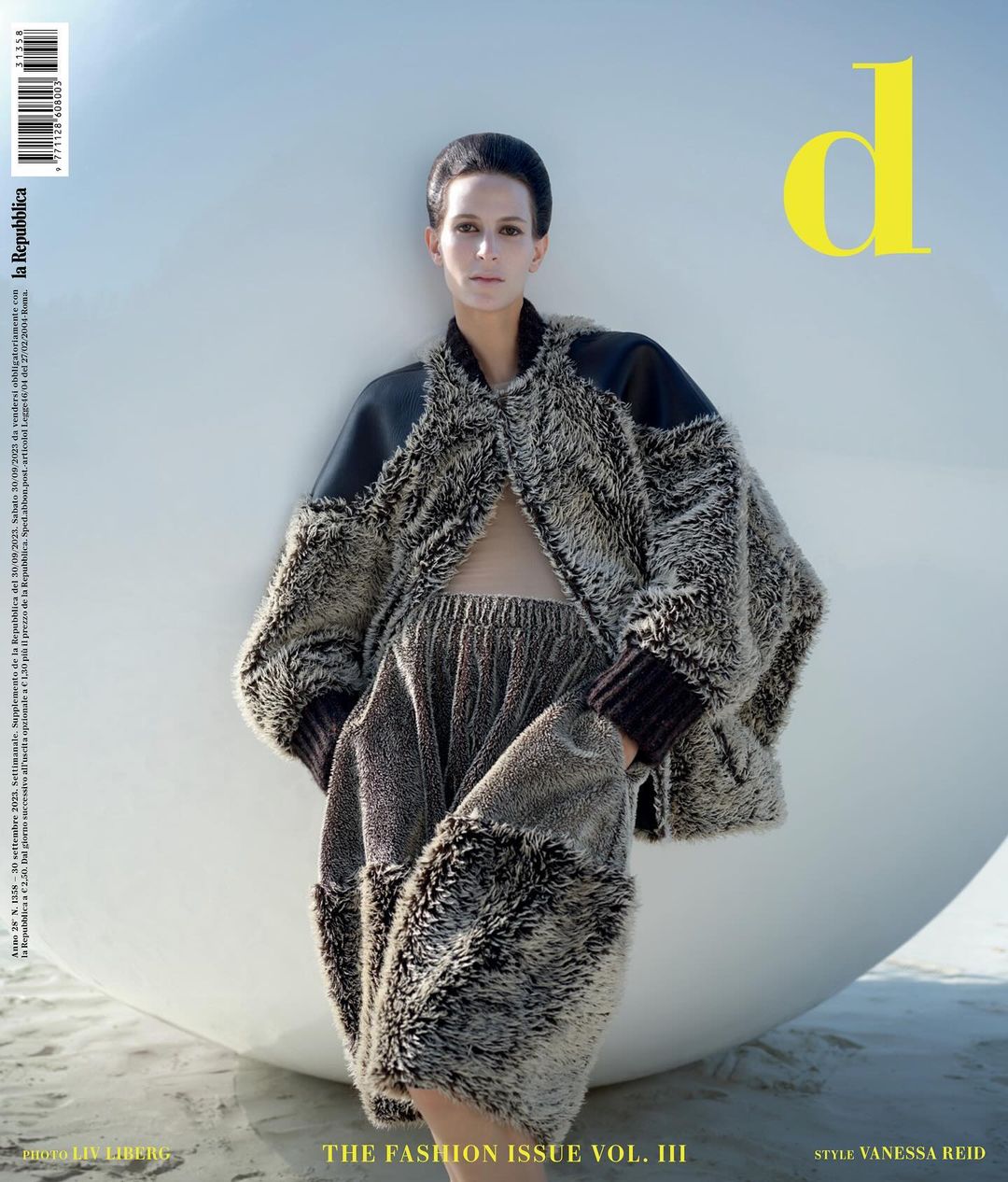 Model wearing a textured fur coat and matching trousers posing against a large white sphere on a beach by Liv Liberg