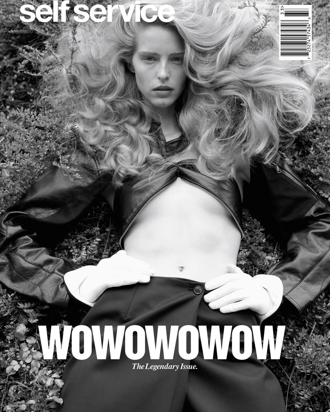 Black and white fashion magazine cover featuring a blonde woman in a black outfit, lying on a bed of green plants, with 'WOWOWOWOWOW' text.