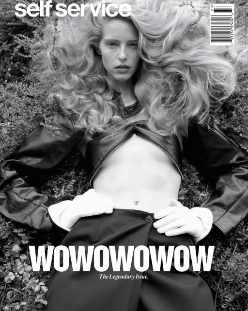 Black and white fashion magazine cover featuring a blonde woman in a black outfit, lying on a bed of green plants, with 'WOWOWOWOWOW' text.