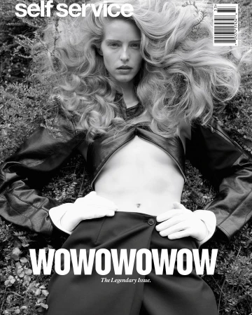 Black and white fashion magazine cover featuring a blonde woman in a black outfit, lying on a bed of green plants, with 'WOWOWOWOWOW' text.