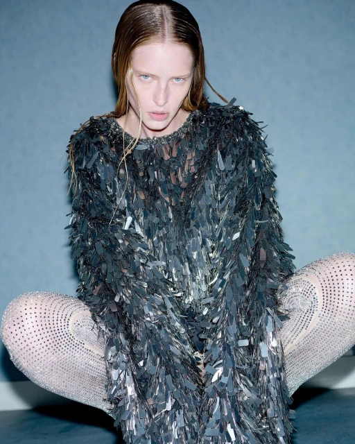 Adult female fashion model in a sequin dress and legging posing in an indoor photo studio with grey background, medium shot.