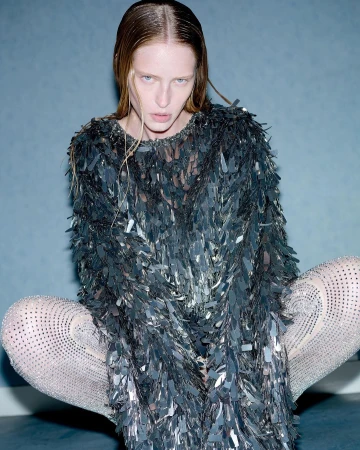 Adult female fashion model in a sequin dress and legging posing in an indoor photo studio with grey background, medium shot.