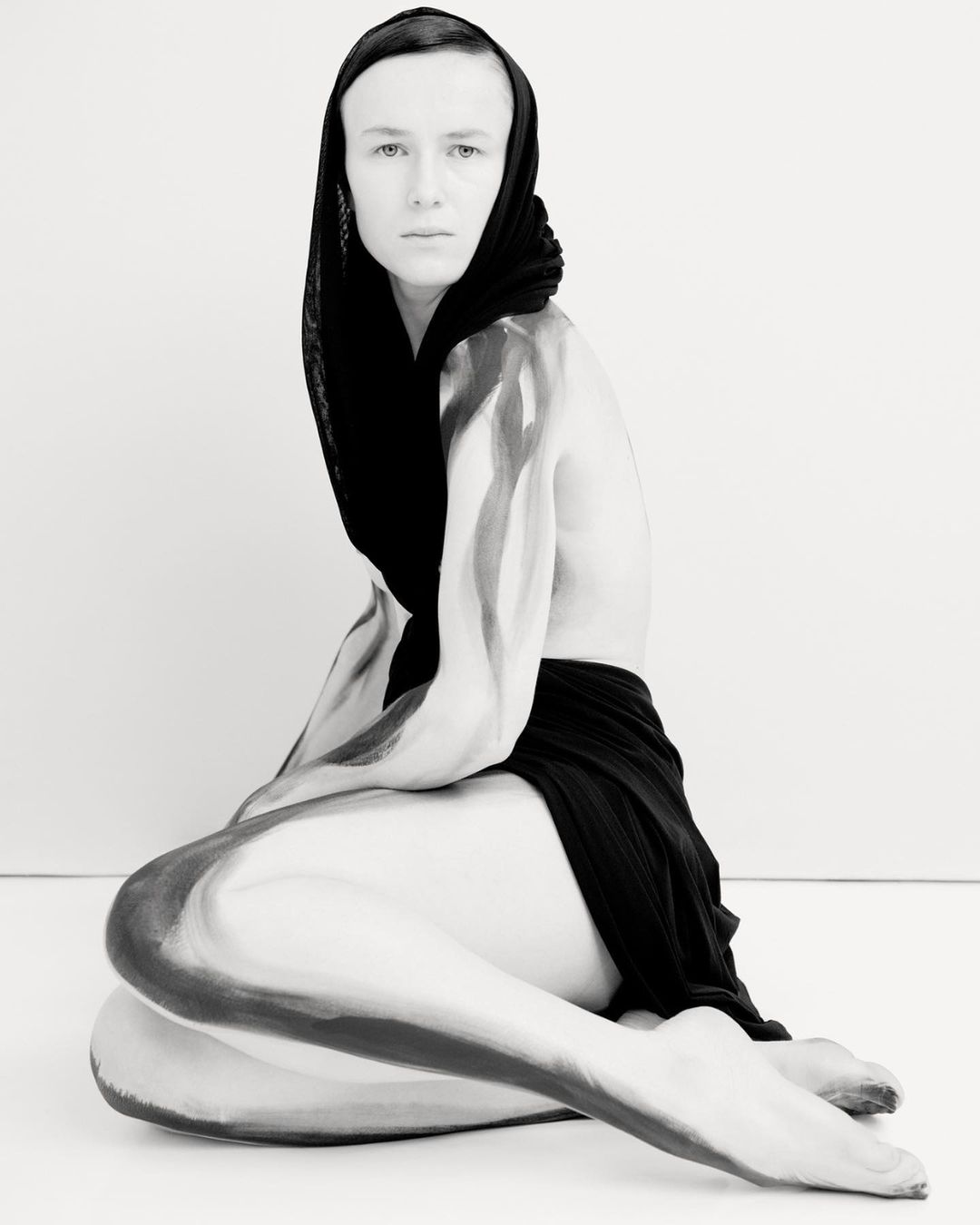 Artistic black and white portrait of a person with body paint, wearing a headscarf, captured in a photo studio setting.