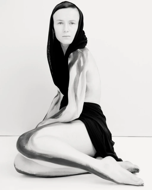 Artistic black and white portrait of a person with body paint, wearing a headscarf, captured in a photo studio setting.