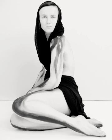 Artistic black and white portrait of a person with body paint, wearing a headscarf, captured in a photo studio setting.