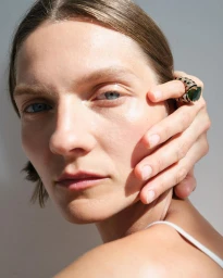 Close up portrait of a woman with a large emerald ring on her hand touching her face photographed by Liv Liberg