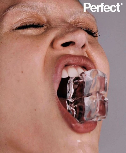 Close-up portrait of a woman with ice cubes in her mouth against a grey background, featuring the "Perfect" logo in the upper right.