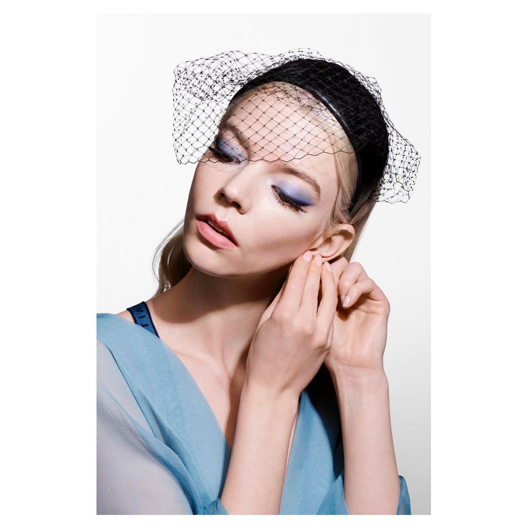 Portrait of a fair-skinned woman with blue eyeshadow and a black veil, posing in front of a white background. Beauty and makeup focus.