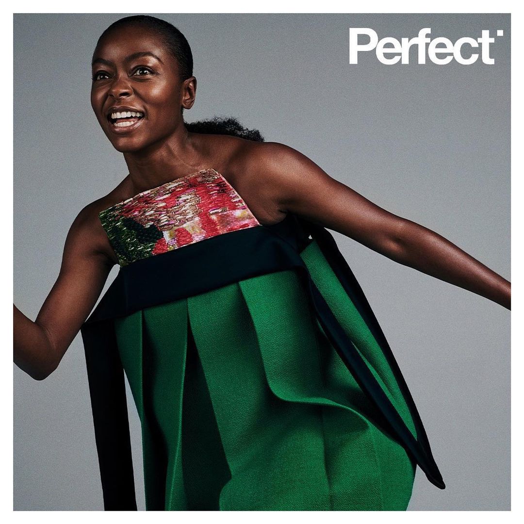 Fashion editorial shot of a Black woman in a green avant-garde dress smiling against a gray background, featuring the text "Perfect."