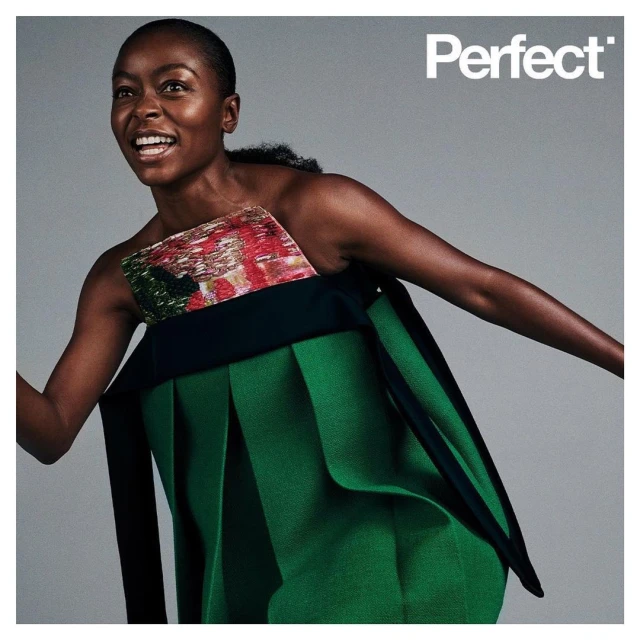 Fashion editorial shot of a Black woman in a green avant-garde dress smiling against a gray background, featuring the text "Perfect."