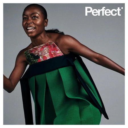 Fashion editorial shot of a Black woman in a green avant-garde dress smiling against a gray background, featuring the text "Perfect."