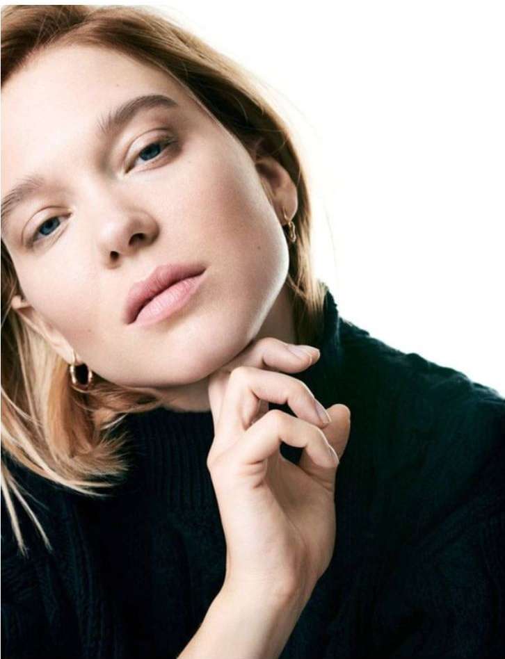 Close-up portrait of a woman resting her chin on her hand, wearing a dark knitted sweater against a bright white background.