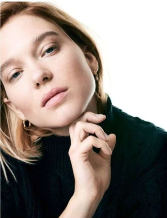 Close-up portrait of a woman resting her chin on her hand, wearing a dark knitted sweater against a bright white background.
