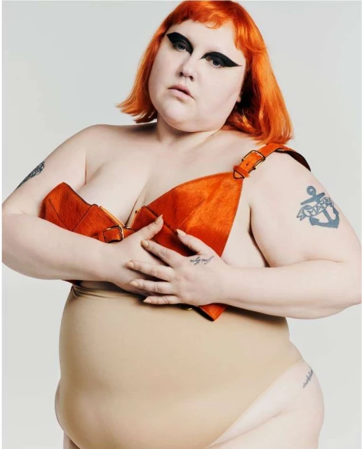 Plus-size woman with bright orange hair and creative makeup in an eye-level portrait in a studio against a white background.