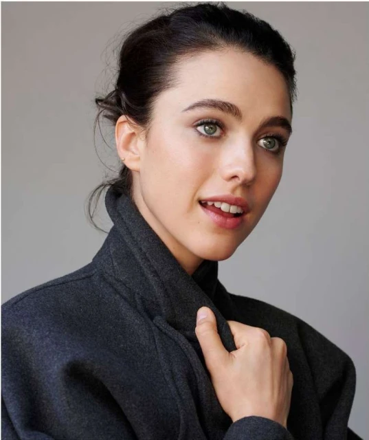 A close-up studio portrait captures a woman with fair skin and dark hair, wearing a charcoal gray coat. She is looking off-camera.